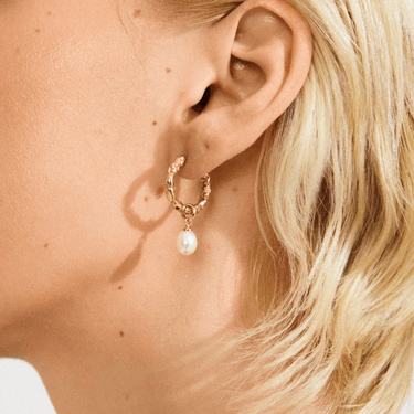 Close-up of a person wearing a gold hoop earring with a pearl pendant.