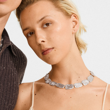 Woman wearing a silver necklace with a plain background