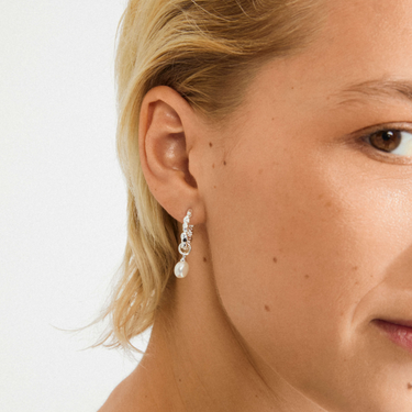 Close-up of a woman wearing pearl earrings with a plain background