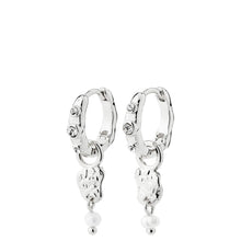 A pair of silver huggie hoop earrings with dangling charms, including a small heart, a textured animal silhouette, and a tiny pearl bead, shown on a plain white background.