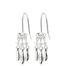A pair of silver drop earrings with textured metal charms, small white pearl beads, and three dangling silver teardrop charms on a plain white background.