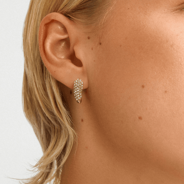 Close-up of an ear wearing a gold earring with a white background