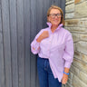 Woman wearing a purple striped shirt and blue jeans standing against a wooden and stone wall.
