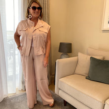 Woman in a light pink outfit standing in a living room with a beige sofa and lamp.