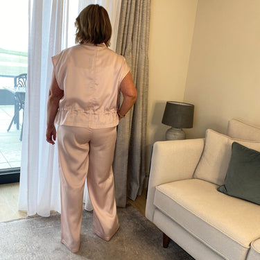 Woman in a beige outfit standing in a living room with a couch and lamp.