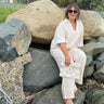 Woman in a white outfit sitting on rocks holding a clutch, with large stones and natural background