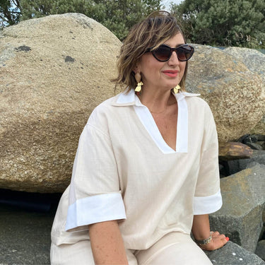 Woman in a beige outfit with white accents sitting on rocks outdoors