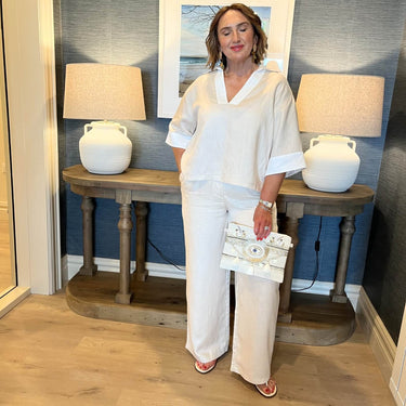 Woman in a white outfit standing in a room with lamps and a painting.