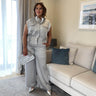 Woman in a light gray outfit standing in a living room with a couch and framed picture.