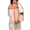 A woman wearing a cream knit sweater and matching skirt, wrapped in a thick fuzzy scarf with orange, beige, gray, and black stripes and fringe.