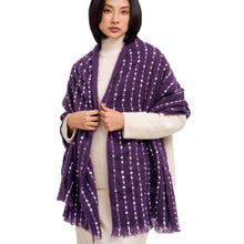 A model wearing a purple open-front shawl with white vertical dotted stripes and fringed edges, layered over a cream ribbed turtleneck sweater against a plain white background.