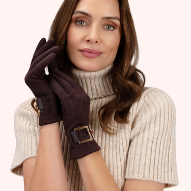 Woman wearing a beige turtleneck sweater and dark brown gloves with a gold buckle on a white background