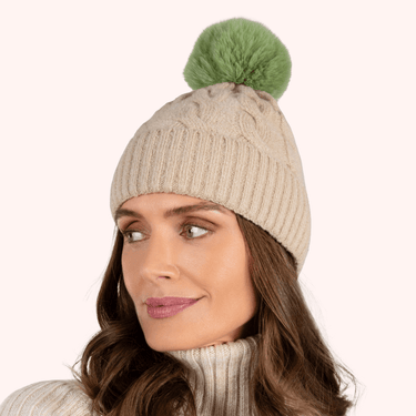 Woman wearing a beige knit beanie with a green pom-pom on a white background