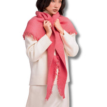 A model wearing a soft pink fringed scarf wrapped around a cream-colored sweater against a plain white background.