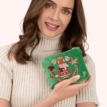 Woman holding a green embroidered pouch with a fox design on a white background
