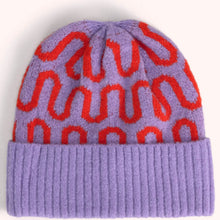 A knit beanie hat in lavender purple with a repeating red wavy pattern and a solid ribbed purple cuff, shown against a plain light background.