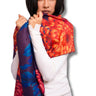 A woman wearing a white long-sleeve top models a vibrant floral shawl with a bold red, orange, and blue chrysanthemum pattern against a plain white background.