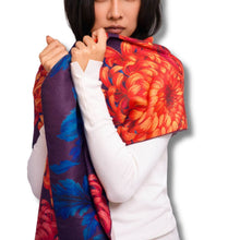 A woman wearing a white long-sleeve top models a vibrant floral shawl with a bold red, orange, and blue chrysanthemum pattern against a plain white background.