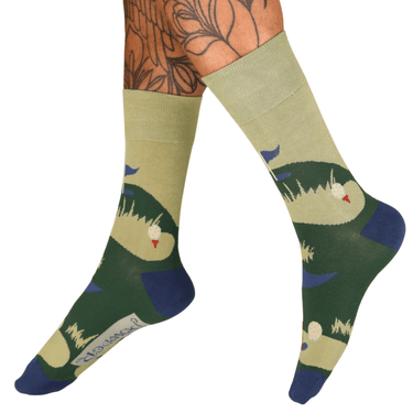 Green and beige socks with nature-themed design worn by a person with tattoos.