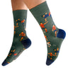 A pair of crew socks worn on a person's feet, shown against a plain white background. The socks are dark green with a pattern of stylized soccer players in orange, blue, and white, with solid dark blue heels, toes, and cuffs.