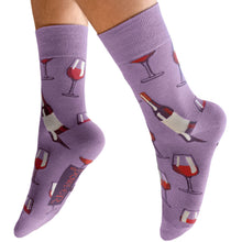 A pair of lavender crew socks with a wine-themed pattern of wine glasses, bottles, and a wine label, shown on a person's feet against a white background.