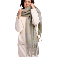 A woman wearing a cream ribbed knit sweater and matching skirt, wrapped in a sage green fringed scarf with subtle multicolor flecks, against a plain white background.