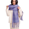 A model wearing a soft, textured knit scarf in a lavender-purple color with subtle pink and blue speckled patterns, styled over a cream-colored knit sweater against a solid white background.
