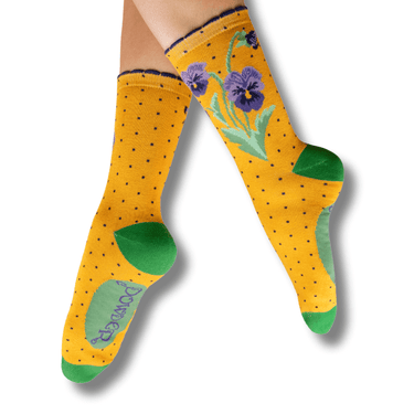 Yellow socks with floral design and green accents worn by a person on a white background