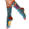 A pair of crew socks worn on a person's feet, featuring a colorful cartoon owl design on a teal blue background with small pink hearts and gold stars. The socks have rust orange cuffs, heels, and toes, and the word 'Pookie' is printed on the sole.