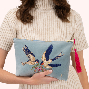 Light blue pouch with embroidered birds held by a person wearing a beige sweater.