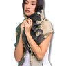 A woman modeling a lightweight scarf with a green, black, and beige camouflage pattern, wrapped around her neck and shoulders against a plain white background.