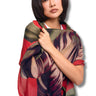 A woman wearing a lightweight patterned shawl draped over her shoulders, featuring a mix of red, olive green, and dark purple tropical leaf motifs, set against a plain white background.