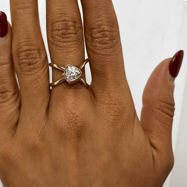 Gold ring with a heart-shaped diamond on a person's finger against a white background