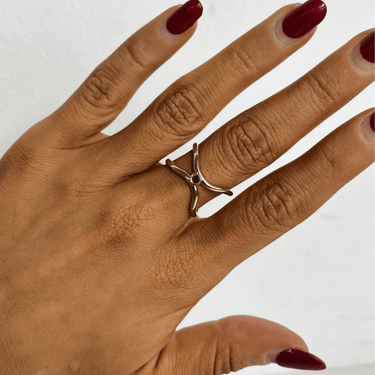 Hand wearing a gold ring with a white stone on a plain background