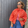 Woman wearing a red polka dot blouse and blue jeans against a wooden wall.