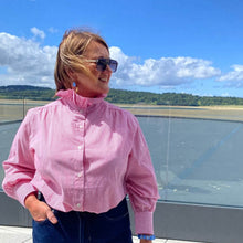 Woman in a pink shirt standing on an airport observation deck with a scenic view.
