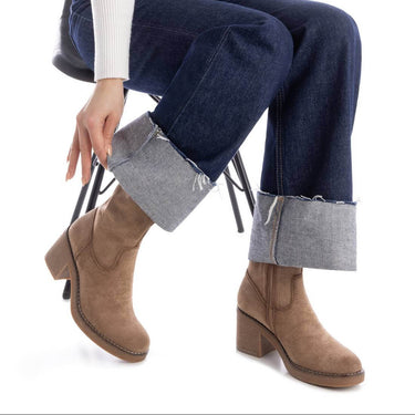 Person wearing brown ankle boots and blue jeans sitting on a chair.
