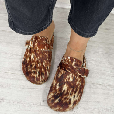 Person wearing leopard print slippers with black pants on a light wooden floor.