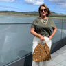 Woman holding a brown bag with gold studs by a waterfront