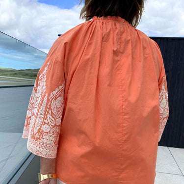 Person wearing an orange blouse with white patterns in a car, with a scenic view outside.