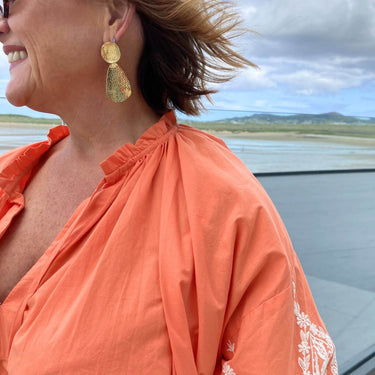 Woman wearing an orange top with a scenic background