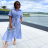 Woman in a light blue dress standing on a rooftop with a scenic view.