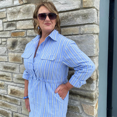 Woman wearing a blue striped dress standing against a stone wall.
