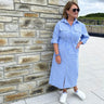 Woman wearing a blue striped dress standing against a stone wall.