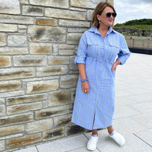 Woman wearing a blue striped dress standing against a stone wall.