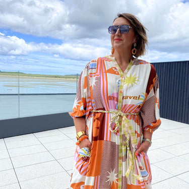 Woman in a colorful dress standing on a rooftop with a scenic view of water and sky.