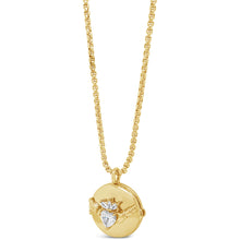 A gold pendant necklace featuring a round gold locket with a winged heart design set with a clear heart-shaped gemstone, suspended from a gold chain on a white background.
