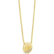 A gold oval pendant necklace with the brand name 'Guess' engraved on the front, accented with small clear stones along the bottom curve, shown on a white background.