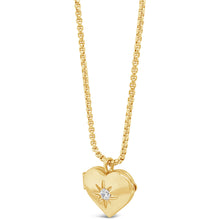 A gold heart-shaped locket pendant necklace with a small clear gemstone in the center, suspended from a gold chain against a plain white background.