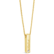 A gold bar pendant necklace with a small clear gemstone and engraved script, hanging from a gold box chain on a white background.